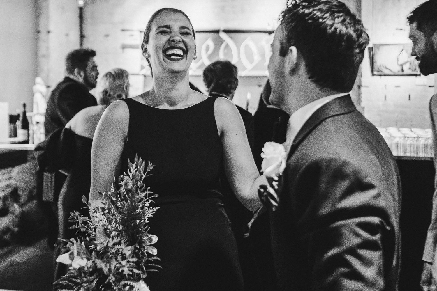A candid black and white moment of laughter during a wedding reception.