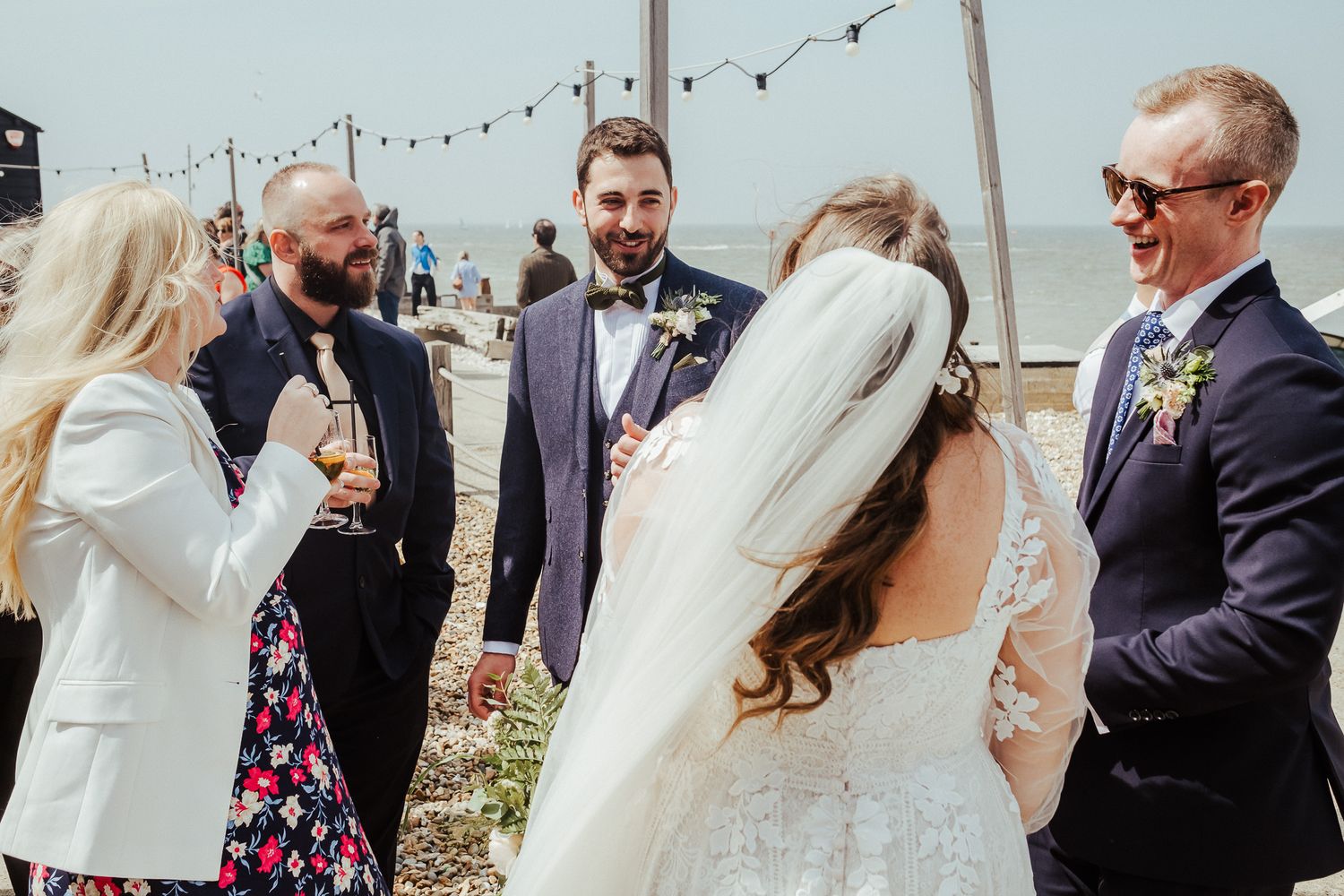 Wedding guests share laughter and conversation under string lights at an outdoor reception.