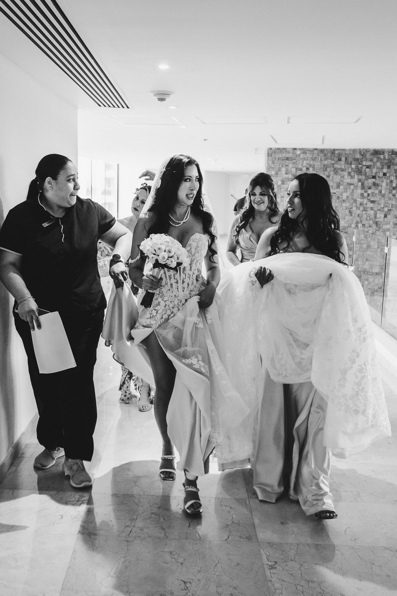 Wedding party walking down a hallway with attendants helping carry a white wedding dress train.