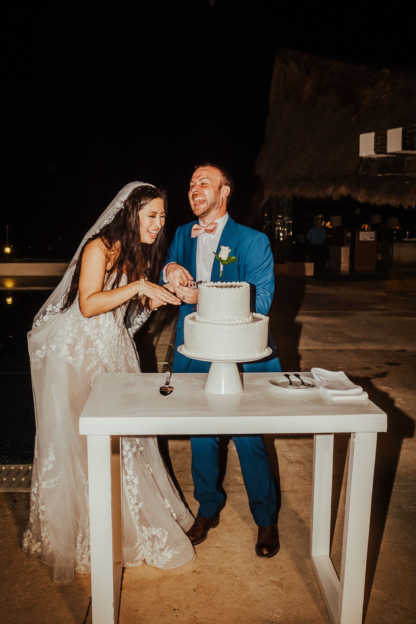 Couple sharing a moment while cutting their wedding cake at an outdoor reception.
