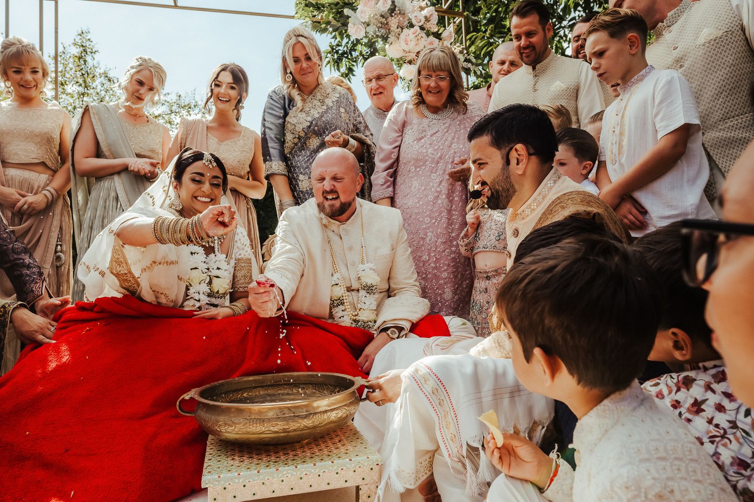 A joyful group gathers around a red-draped table at a festive celebration, sharing laughs and smiles.