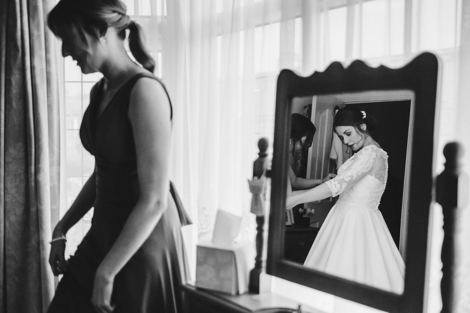 Elegant bridal preparations captured in black and white by a sunlit window.
