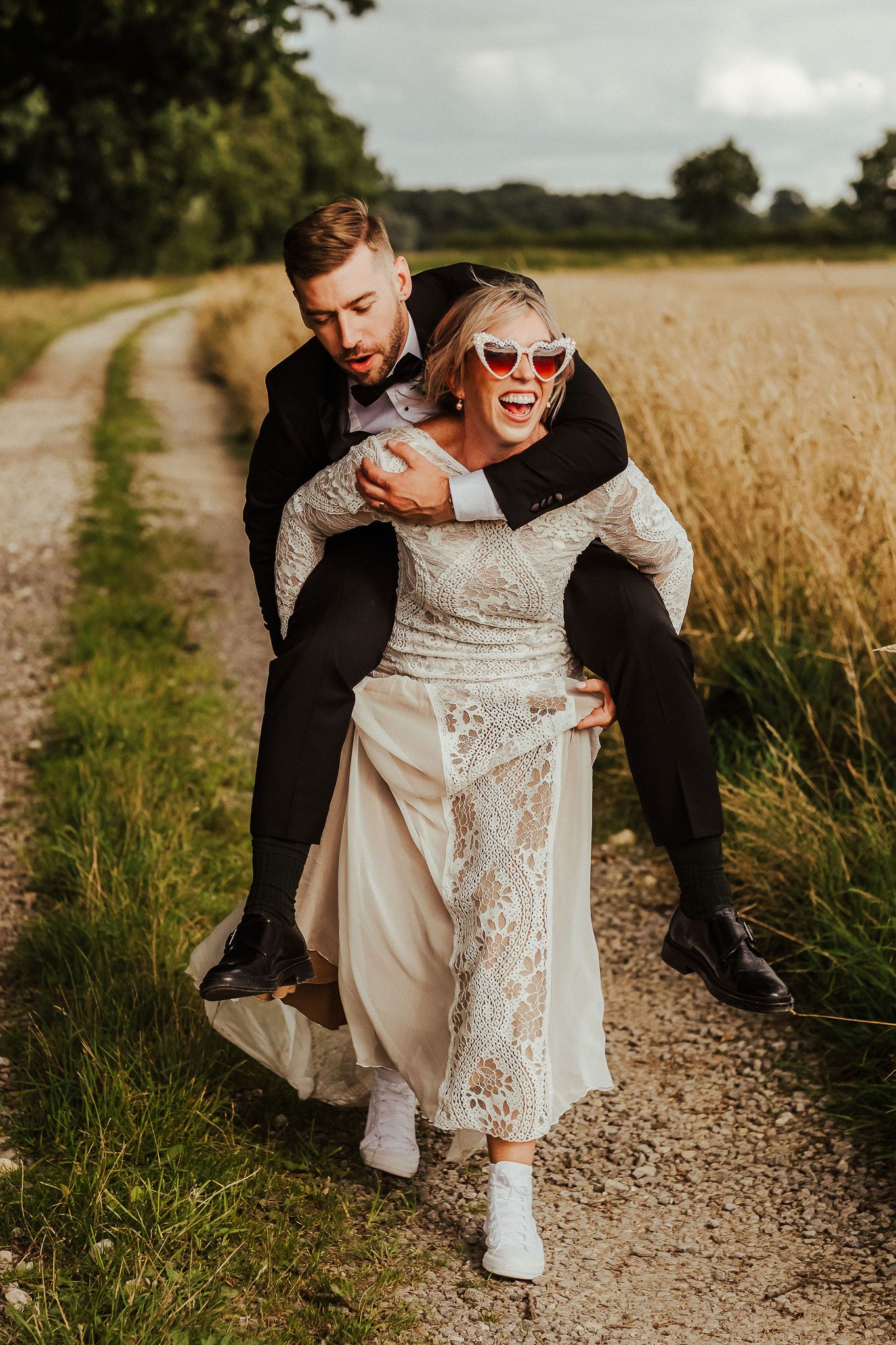 Playful wedding couple having fun on a rural path surrounded by wheat fields.