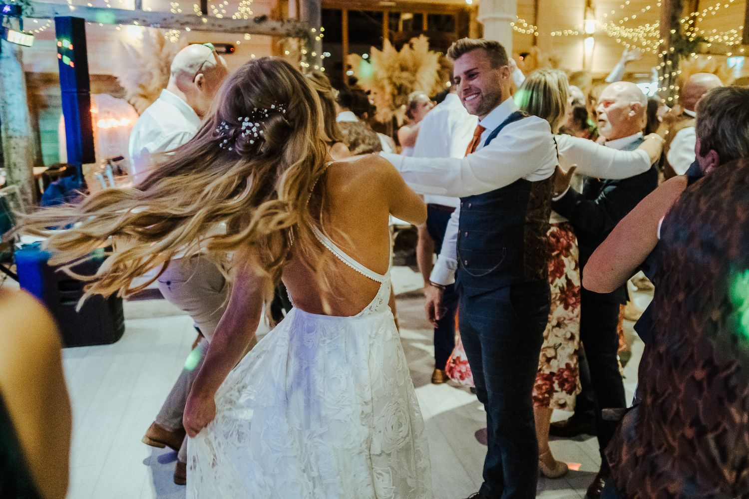 Guests dance and celebrate at a festive wedding reception under warm lighting.