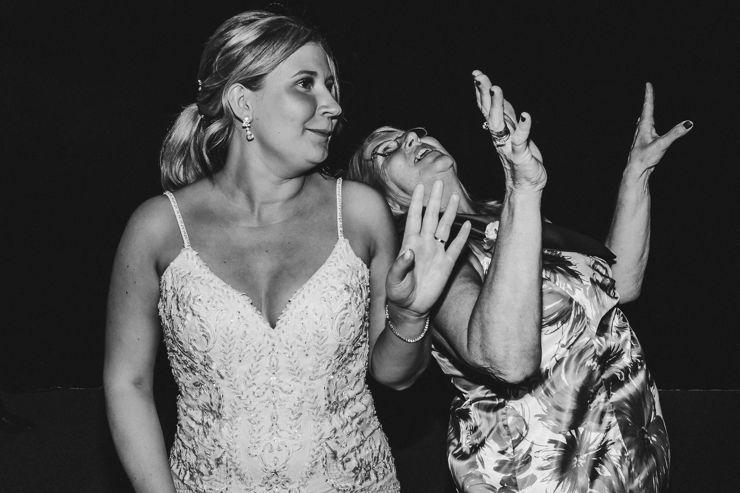 Black and white candid photo shows wedding guests sharing an emotional moment on dance floor.