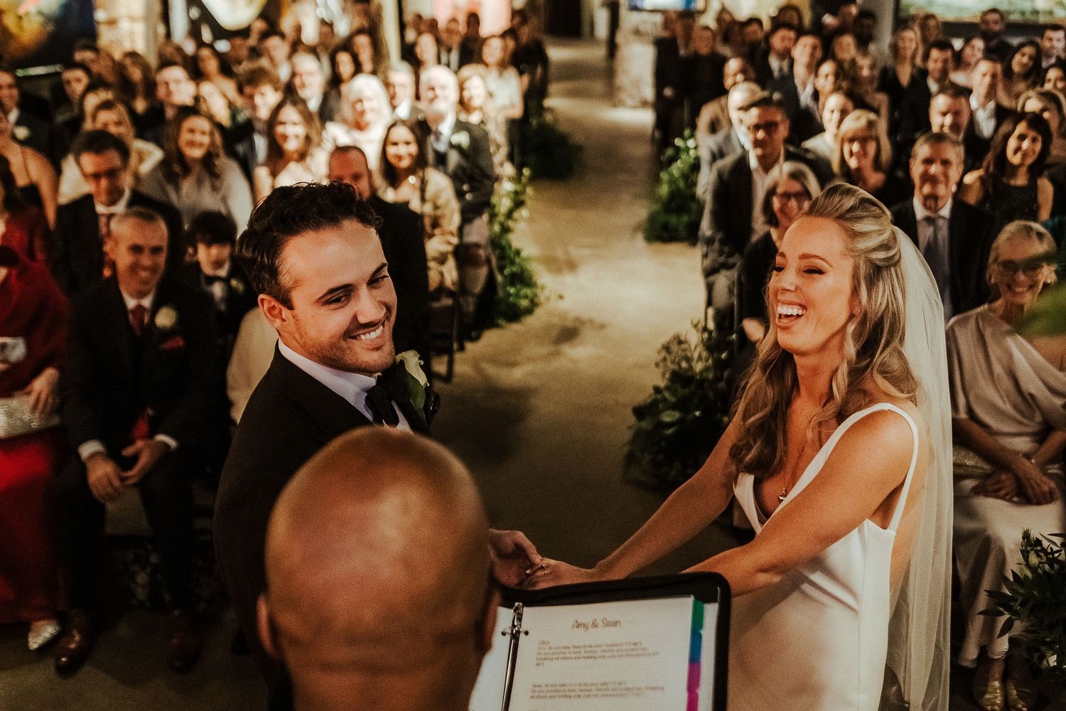 Couple shares joyful moment during wedding ceremony in industrial-style venue.