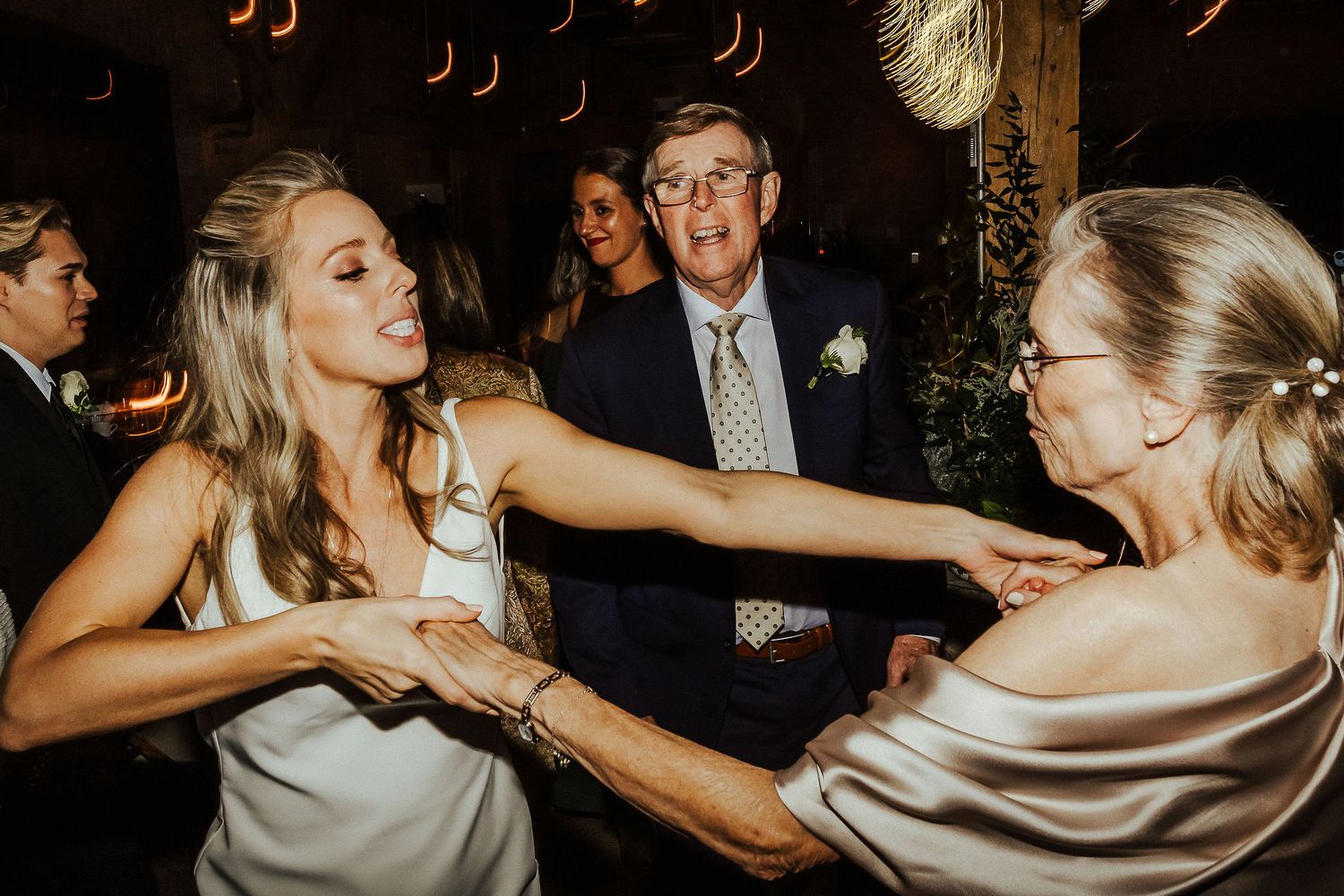 Party guests dancing energetically at a reception with decorative lighting.
