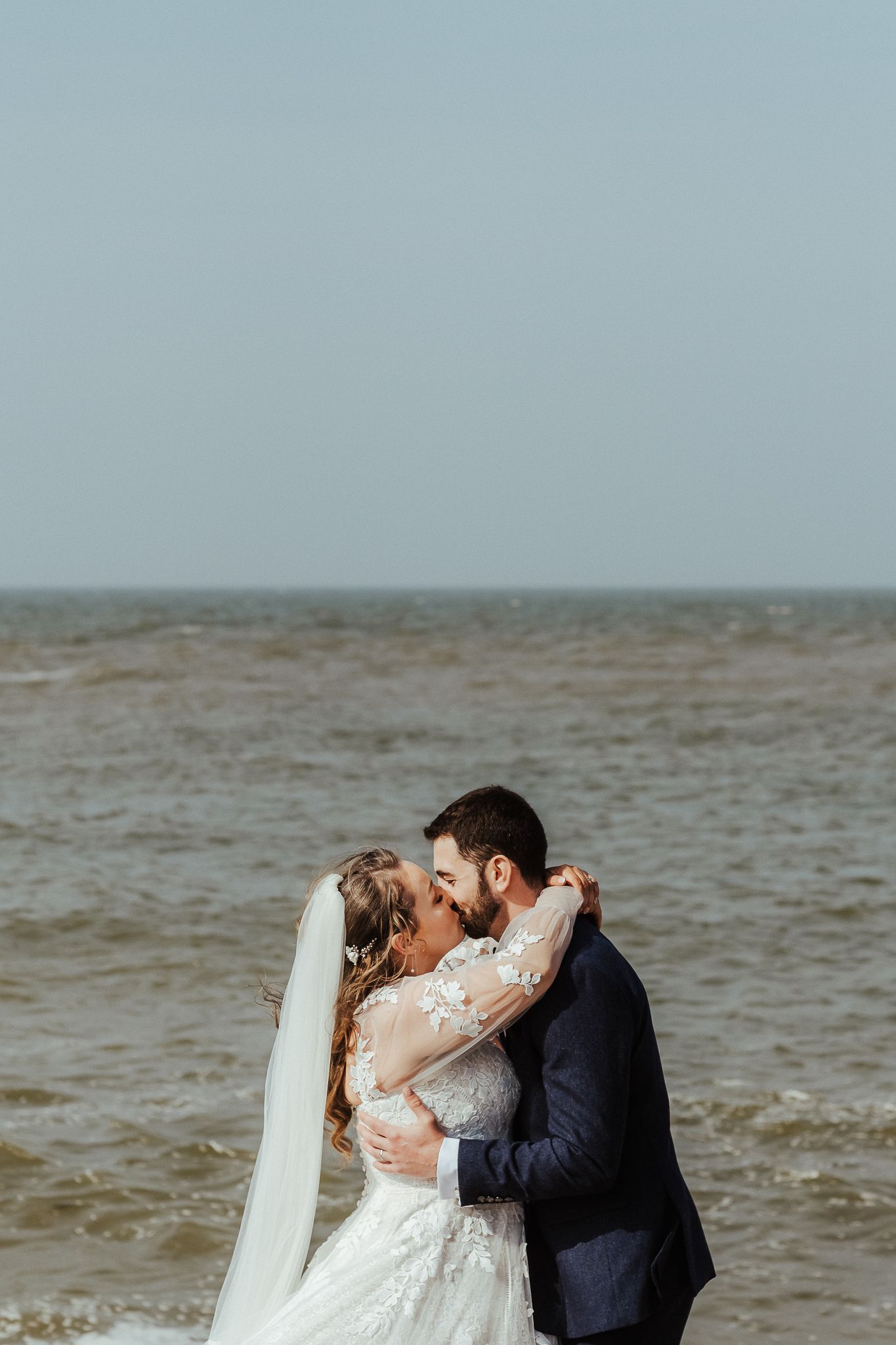 Romantic seaside wedding portrait of couple embracing on a cloudy beach.