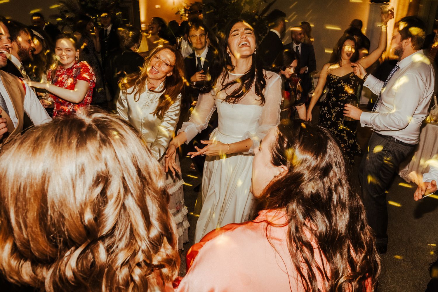 People dancing and celebrating at a joyous reception with warm lighting and festive atmosphere.