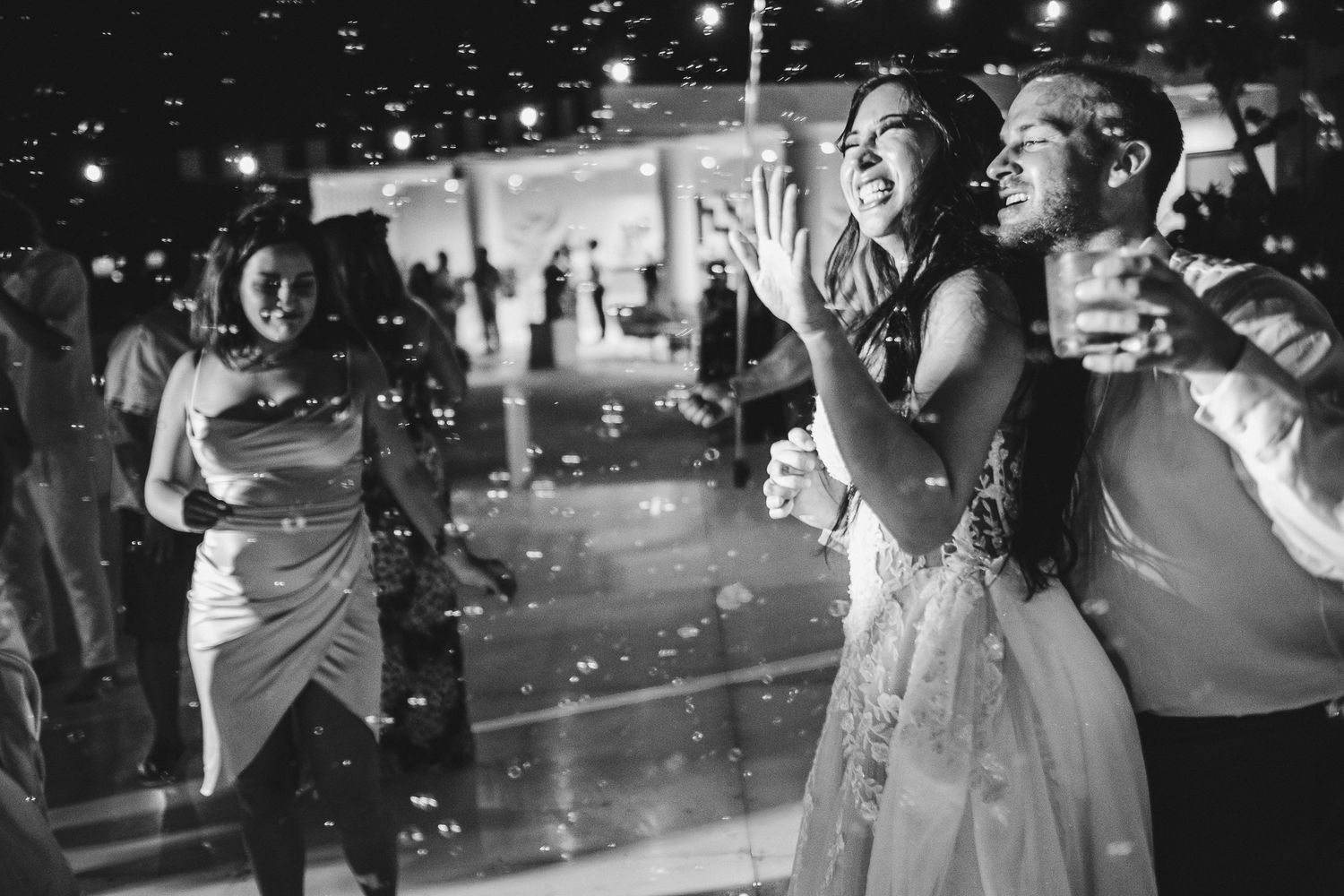 Wedding guests dance under sparkling lights at an evening reception celebration.