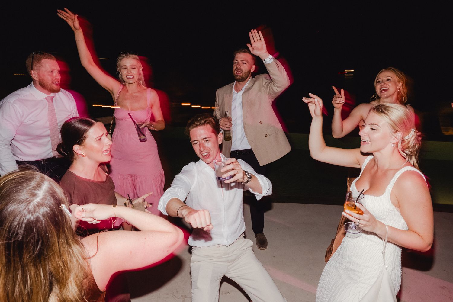 Wedding reception guests dance energetically together on the dance floor at an indoor celebration event.