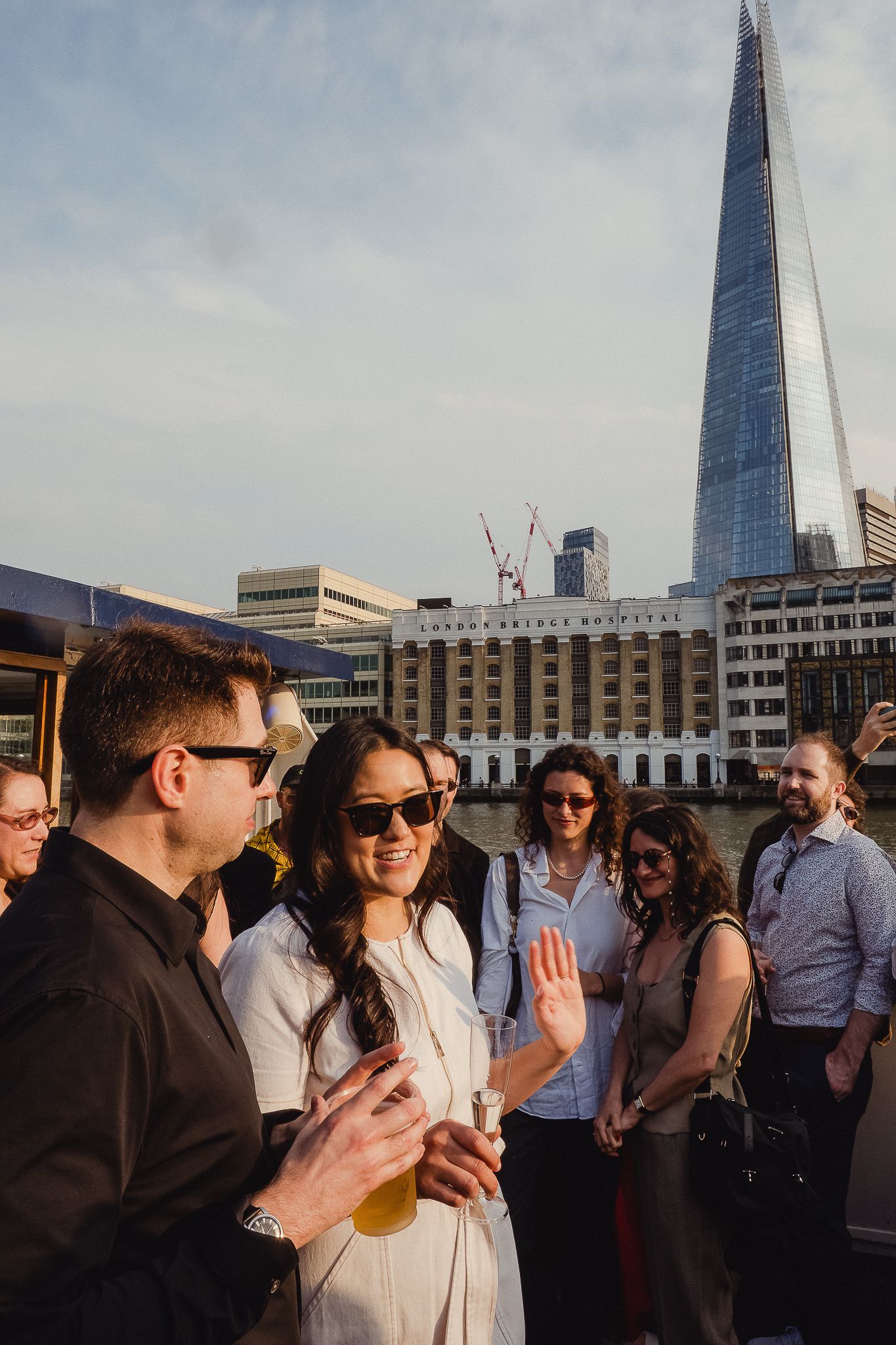 A group of people enjoying drinks and conversation on a rooftop with The Shard building visible in London's skyline.
