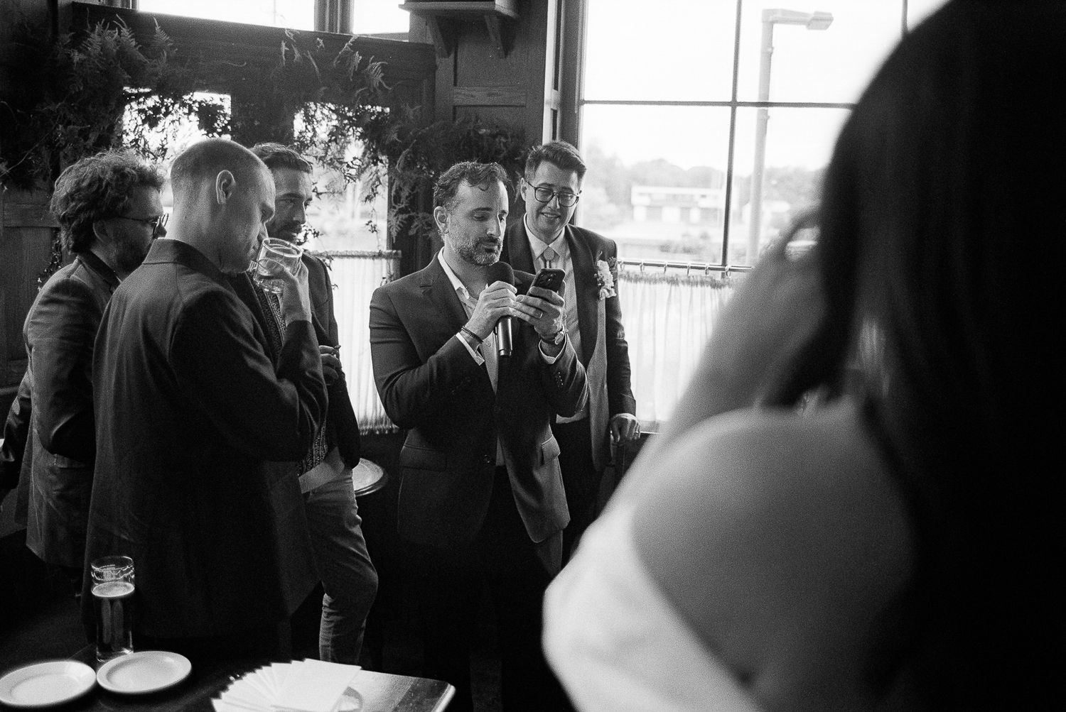 Black and white photo showing a candid moment at a gathering with people mingling and conversing in a social setting.
