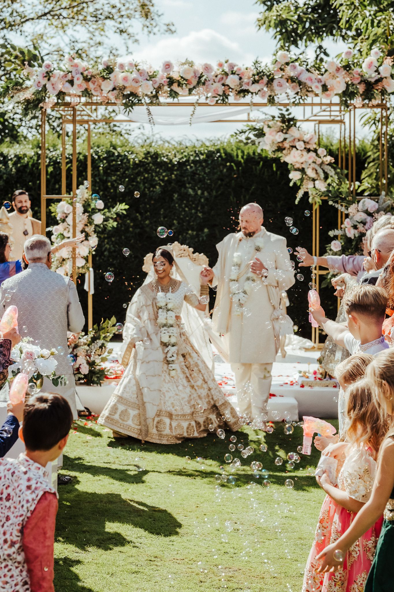 Wedding guests throw confetti in celebration during an outdoor garden reception on a sunny day.