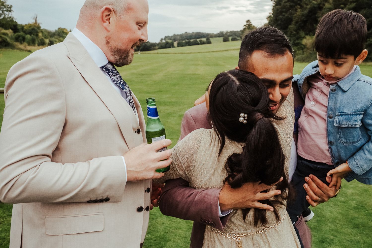 A group of people share a tender moment laughing together on a grassy field on a cloudy day.