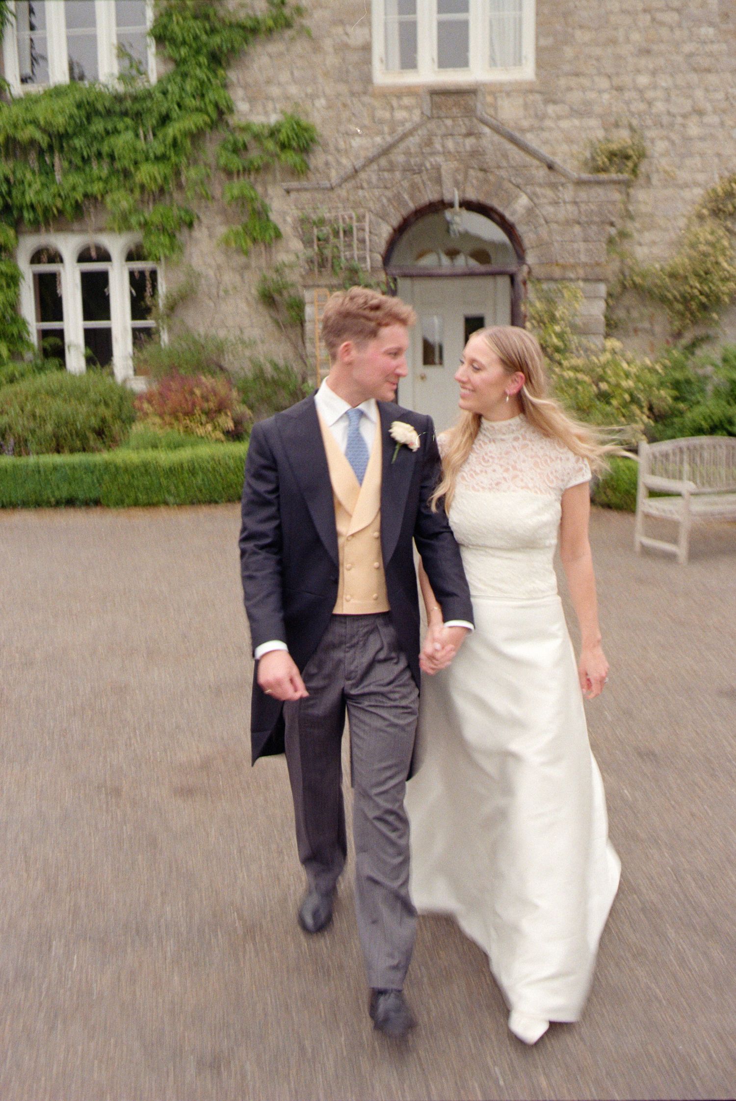 Wedding couple walking together and sharing a playful moment on stone courtyard with historic building backdrop.