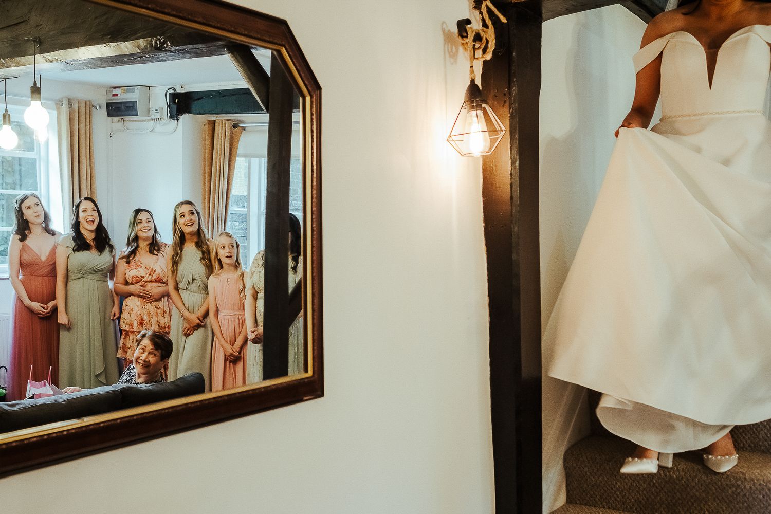 Creative wedding photo showing bridesmaids reflected in mirror while bride stands in doorway.