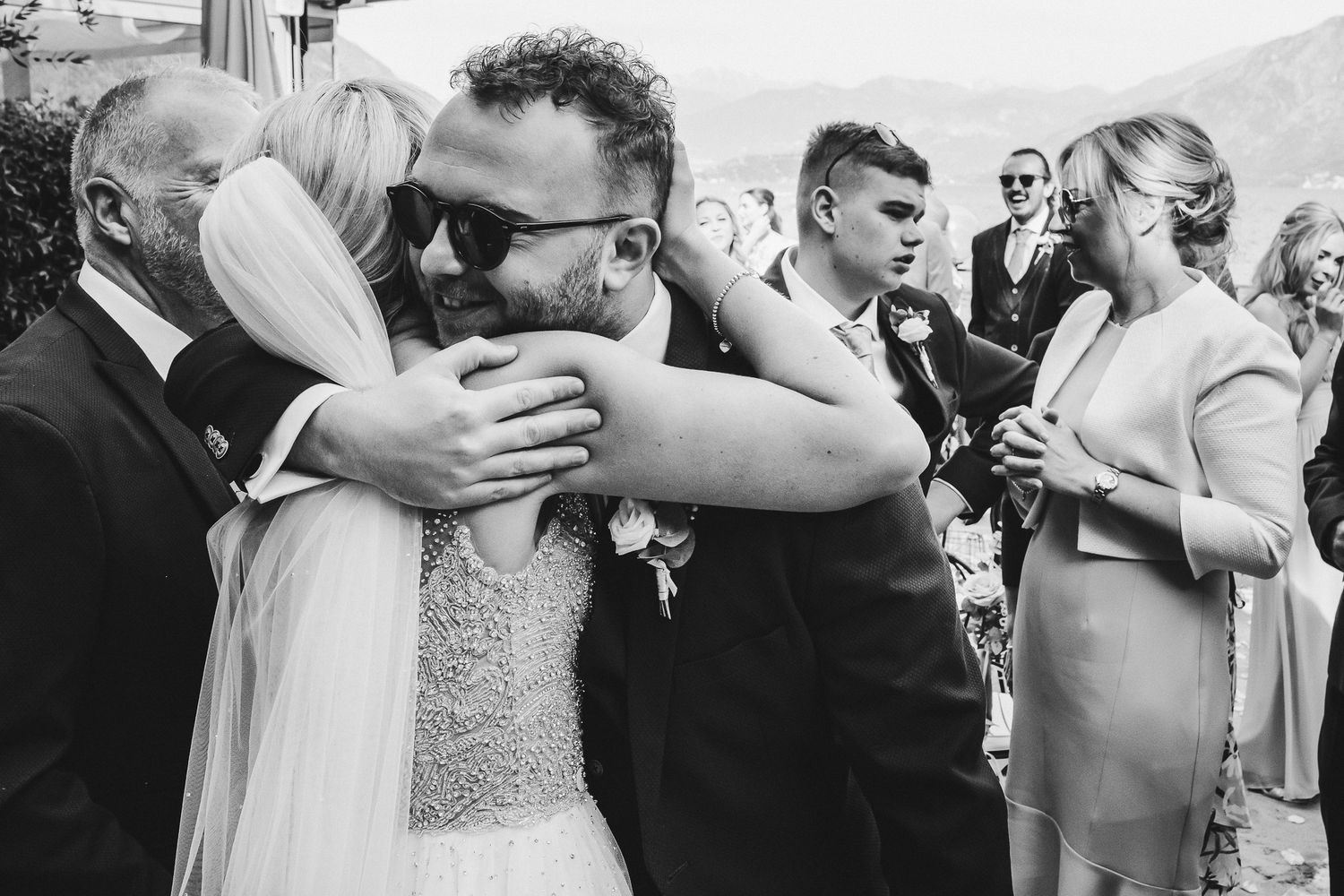 Black and white photo of wedding guests embracing during an outdoor celebration.