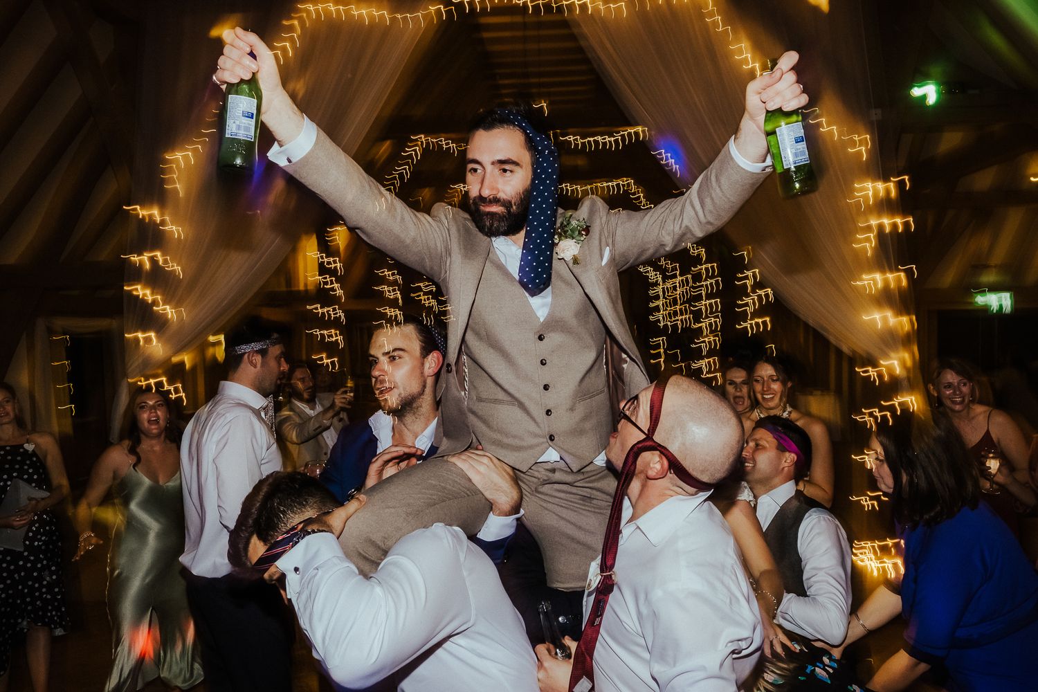 Wedding reception guests dancing and celebrating under warm ambient lighting.