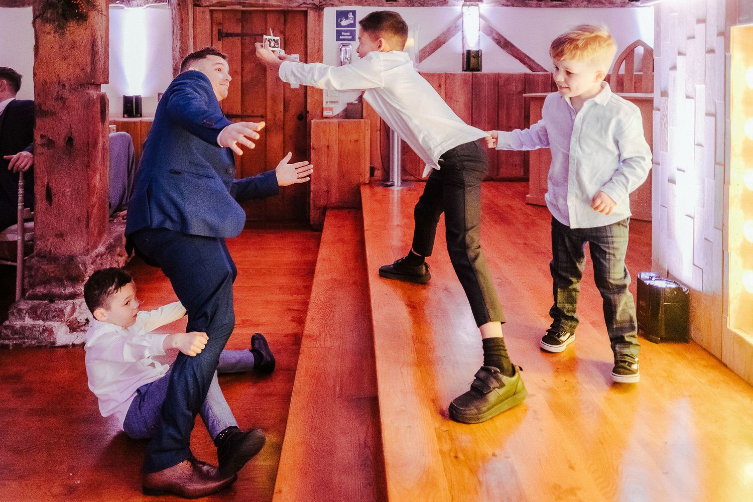 Children and adults dancing energetically on wooden floor at wedding reception.