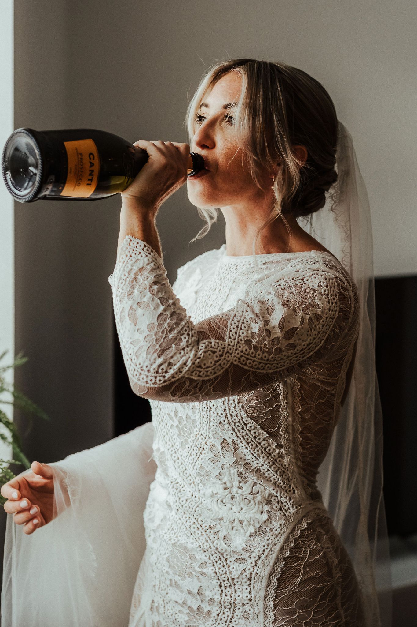Bride in lace wedding dress drinking from champagne bottle in preparation sequence.