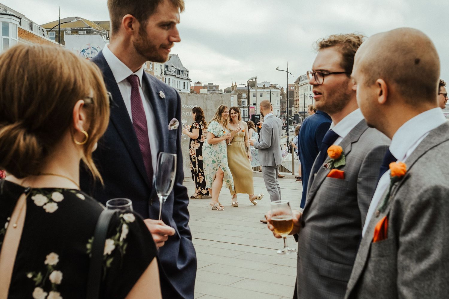 Small group of wedding guests engaged in conversation outside a modern building.