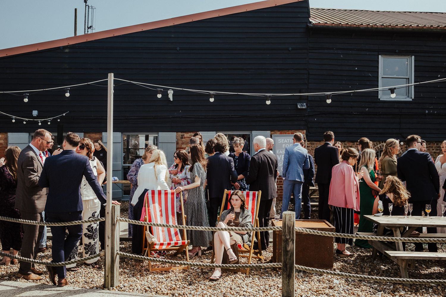Guests gather under string lights at a casual outdoor wedding reception venue.