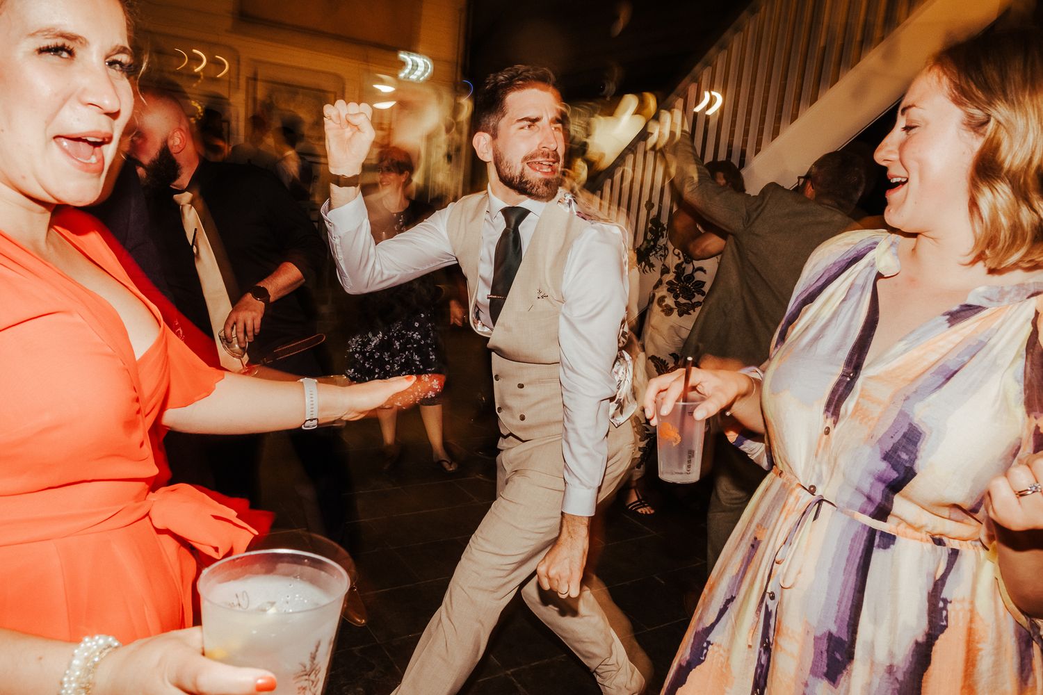 Wedding guests dancing and celebrating at a lively indoor reception party.