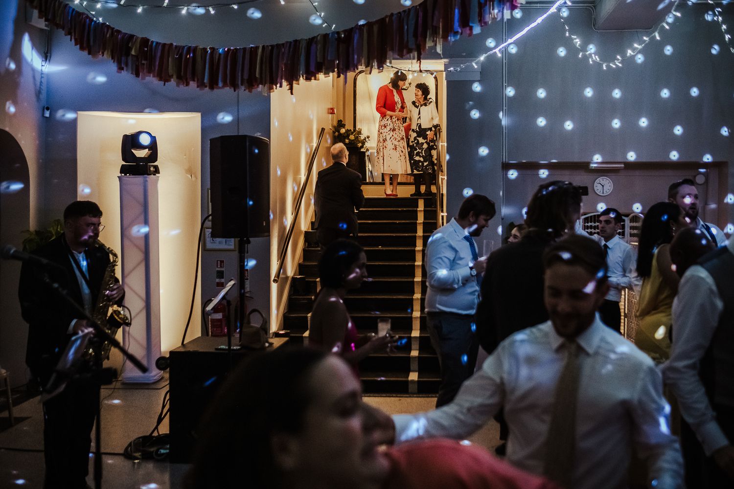 An indoor venue decorated with string lights as guests mingle during an evening celebration.
