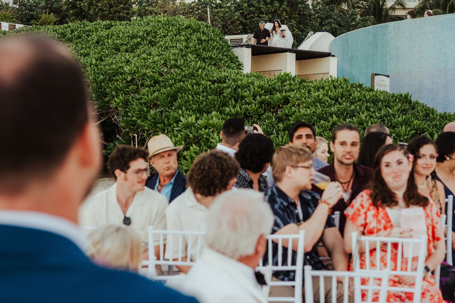 Wedding guests seated in white chairs at an outdoor ceremony venue.