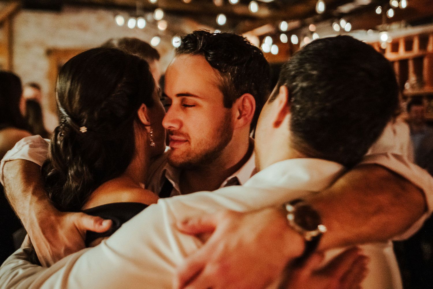 Intimate moment captured at a celebration with warm ambient lighting and string lights overhead.