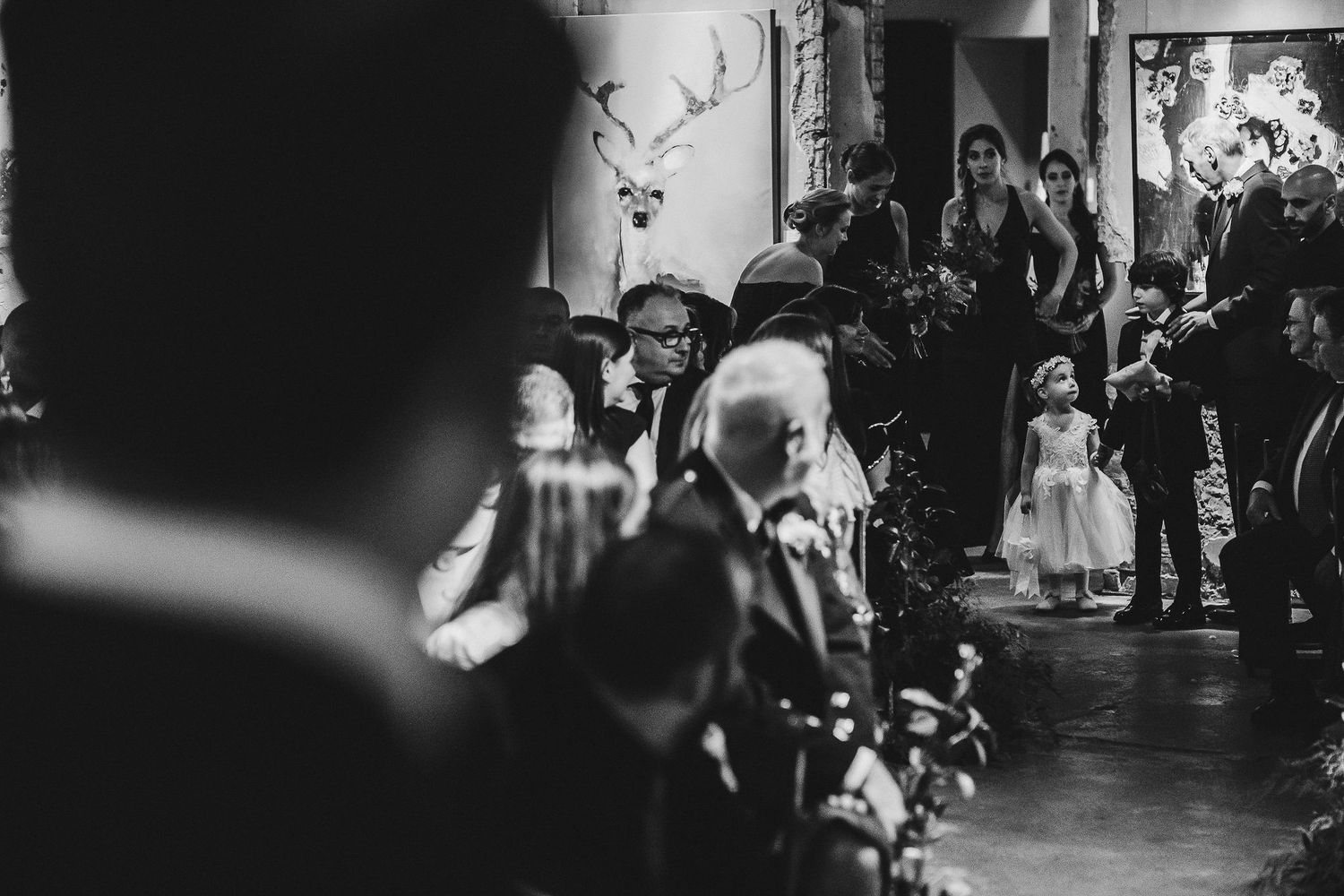 Black and white candid shot of wedding ceremony guests in dimly lit venue.