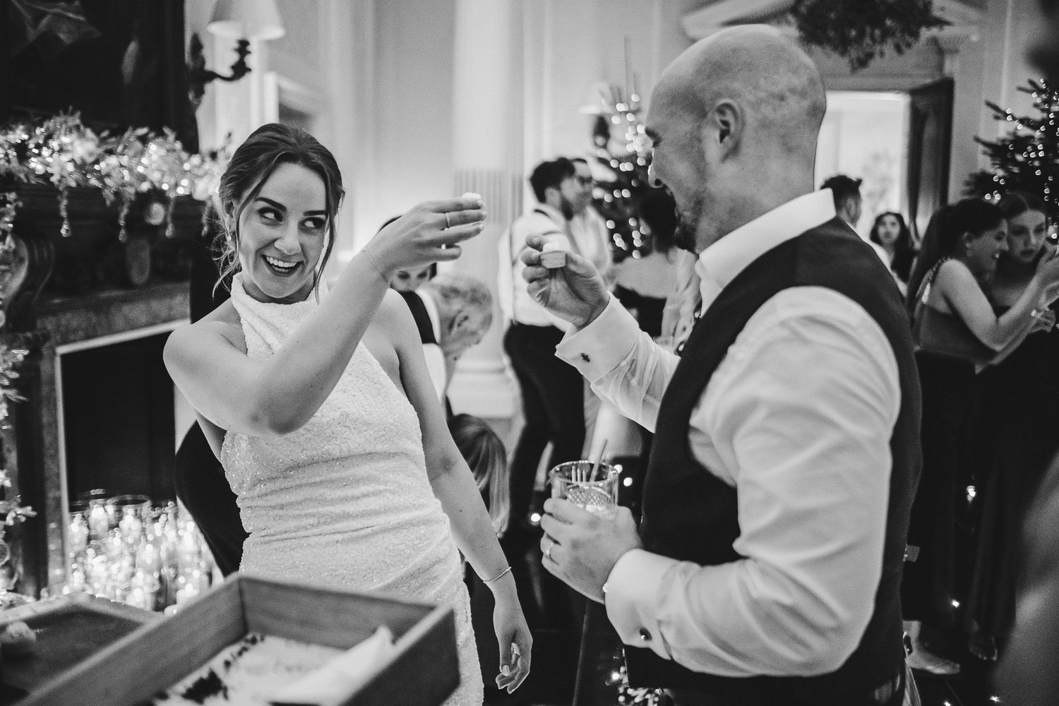 A black and white photo of a wedding celebration with guests toasting drinks at an indoor reception.