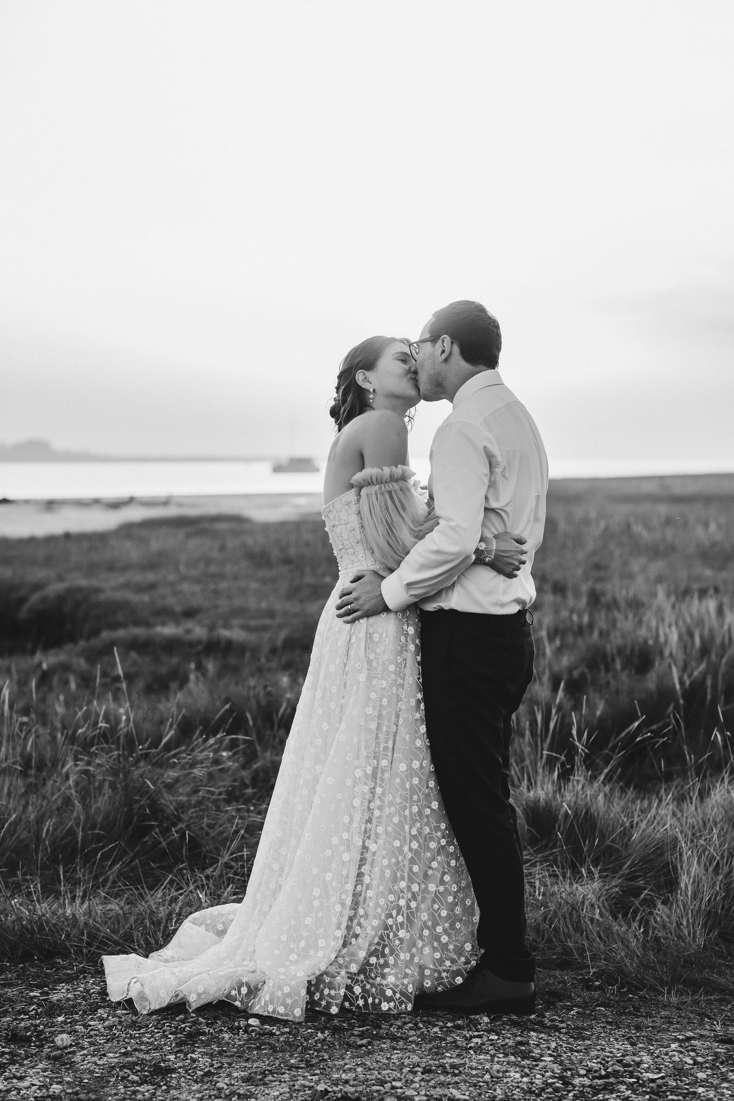 A black and white romantic moment between newlyweds standing in an open field.