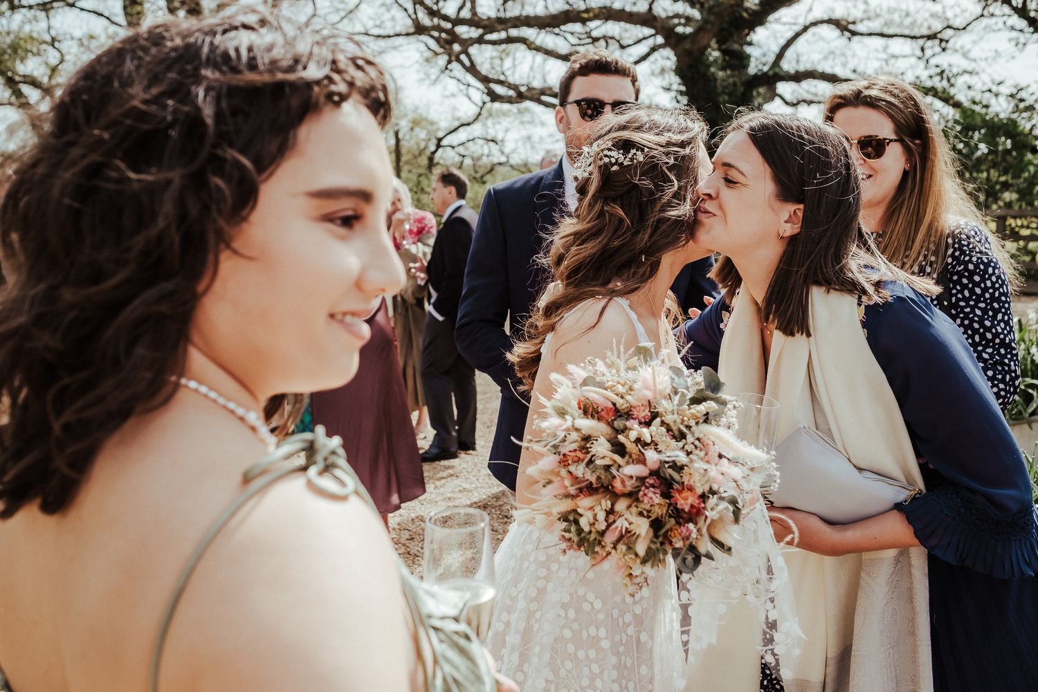 Wedding guests gather outdoors for candid celebration photos with bouquets and smiles.