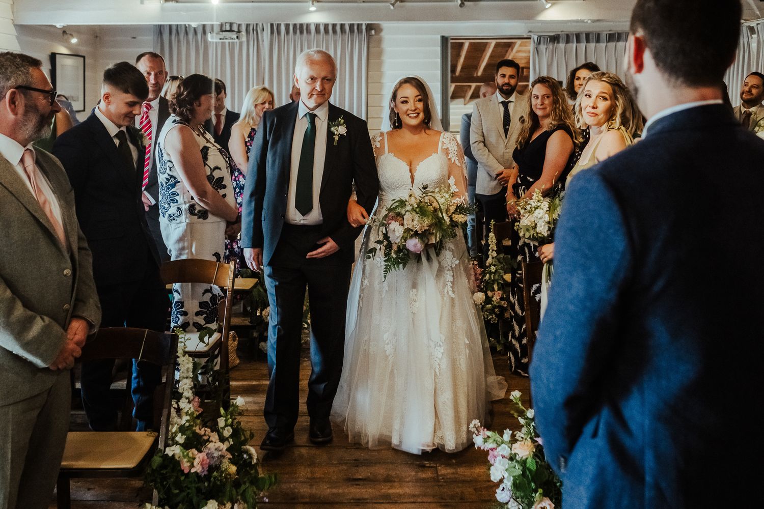 An indoor wedding ceremony with floral arch decorations and guests seated in rows.