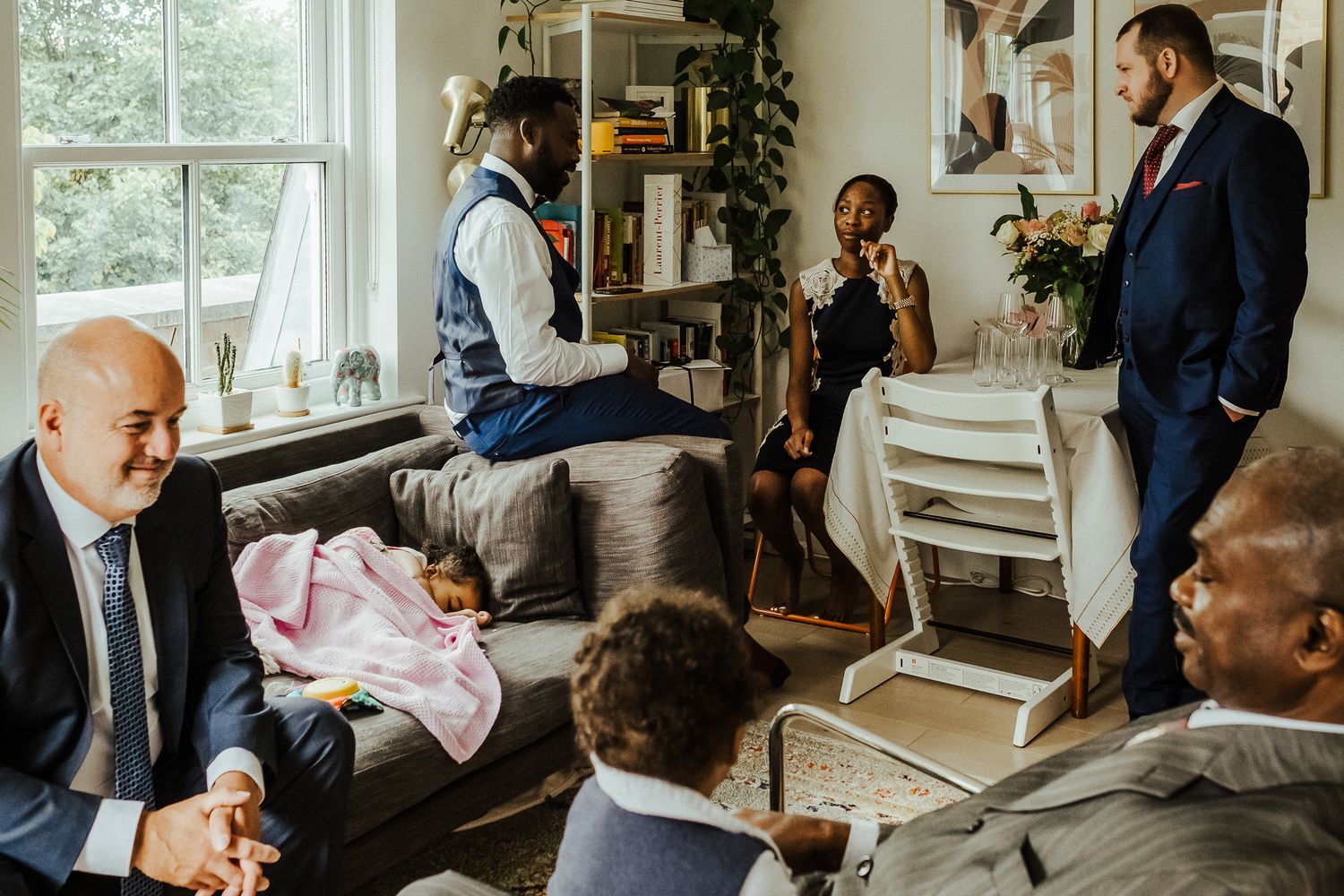 Casual gathering in bright living room with people seated on furniture.
