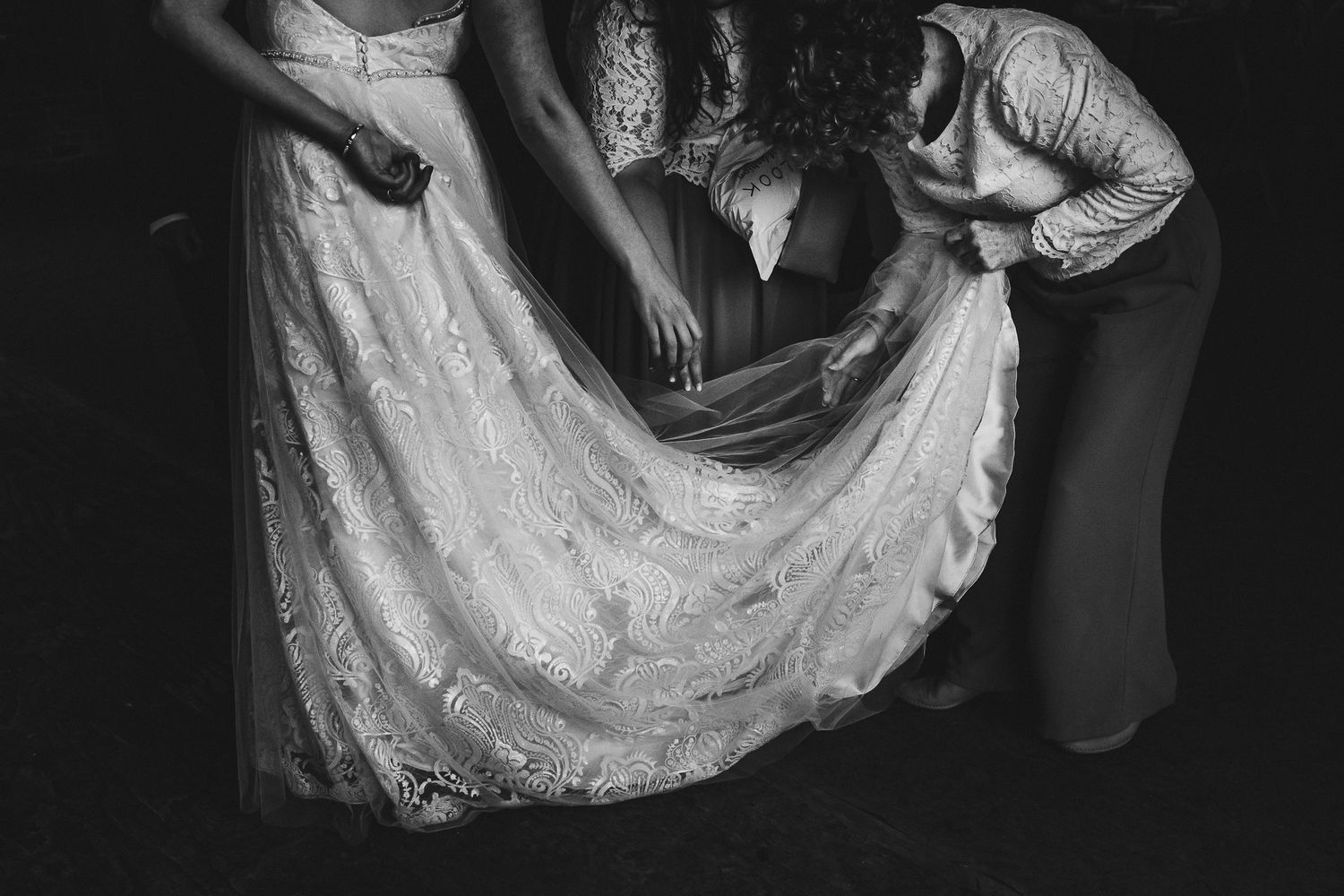 Wedding dress hemline being adjusted by helpers in a black and white shot.