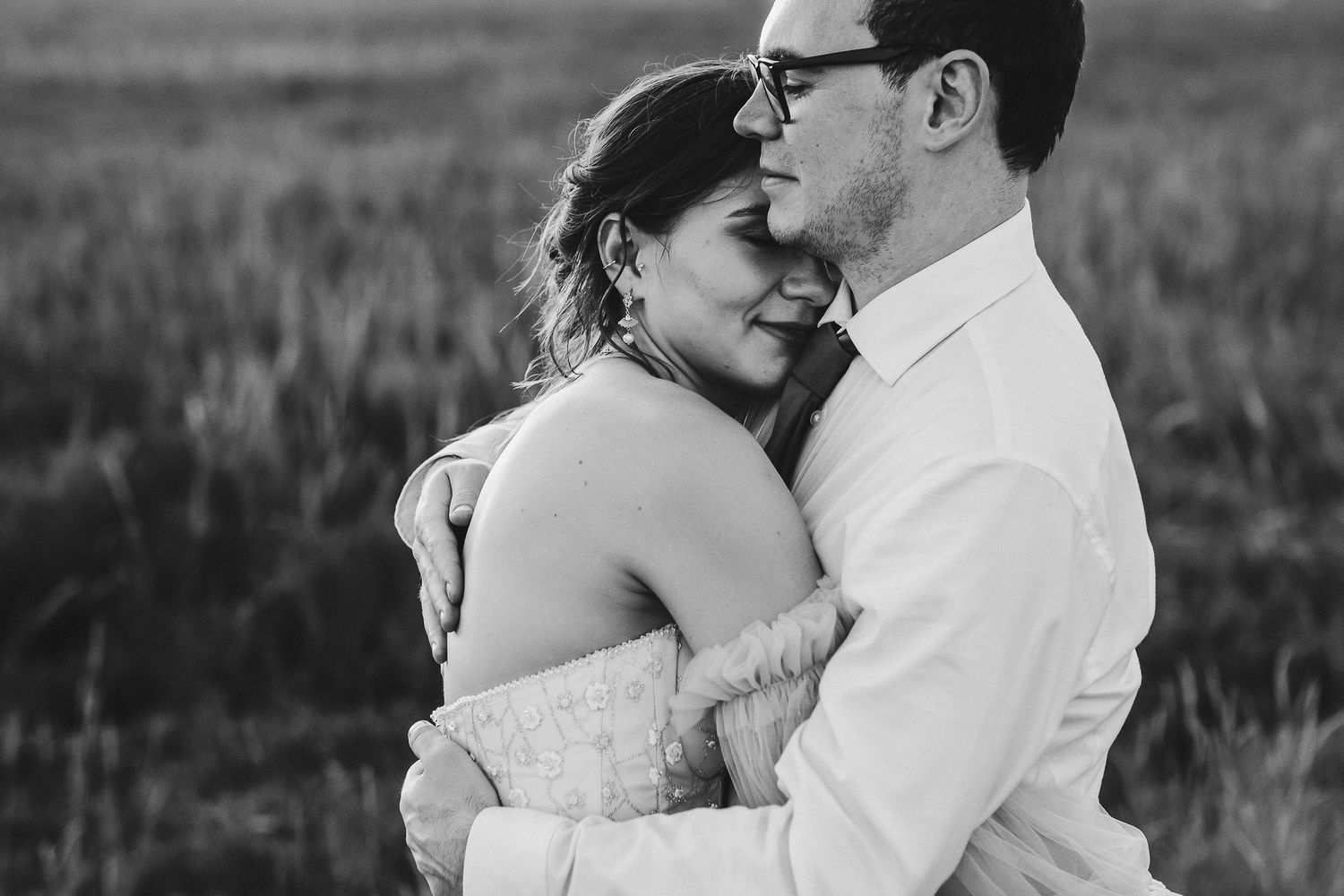 An intimate black and white portrait of a couple embracing in a sunlit field.