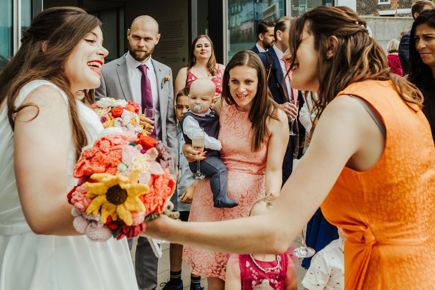 Wedding guests admire a colorful bouquet during an outdoor celebration.