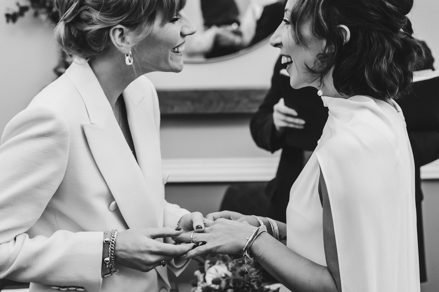 Black and white candid moment of two people in white suits sharing an intimate conversation.