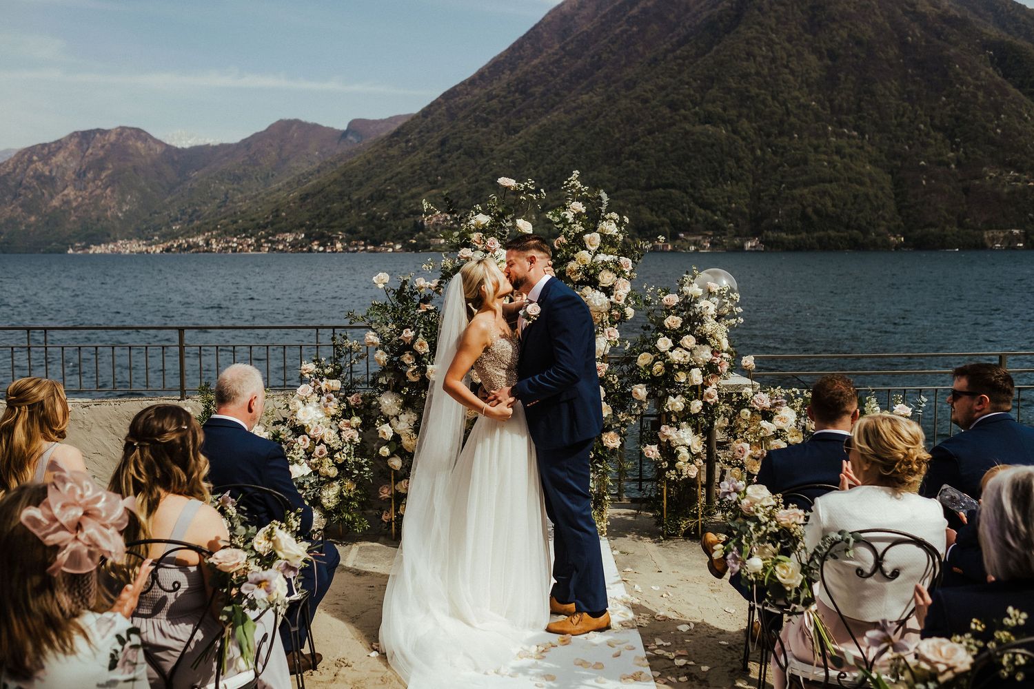 Couple exchanges vows under floral arch with scenic mountain lake backdrop.