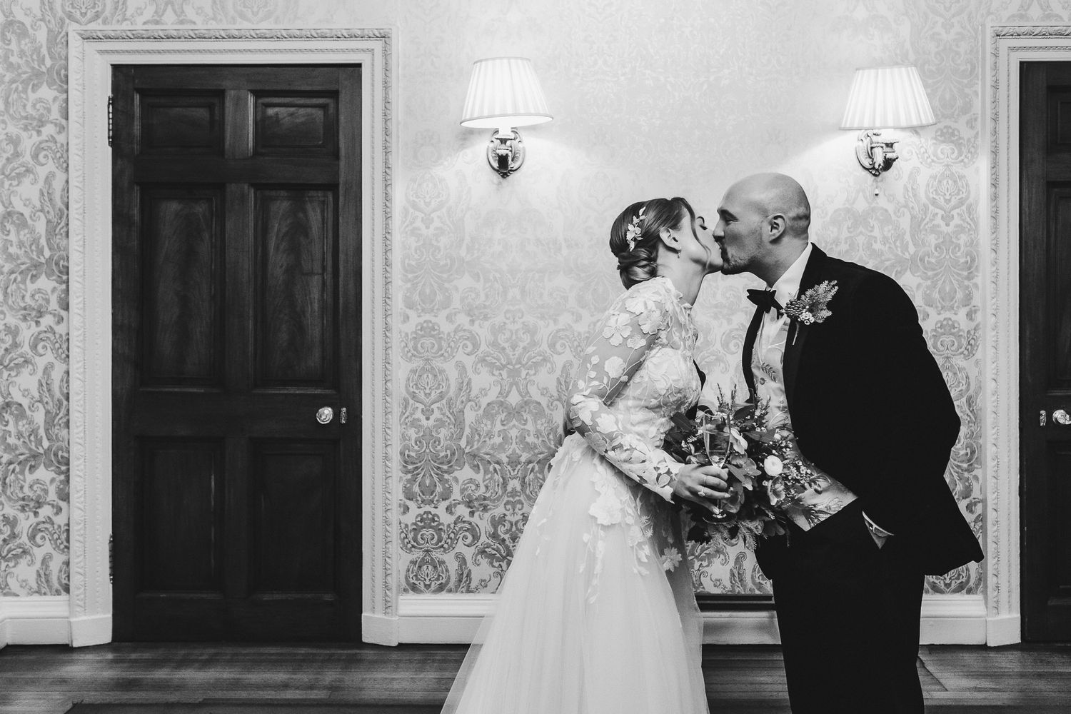 Black and white romantic wedding portrait against vintage wallpaper.