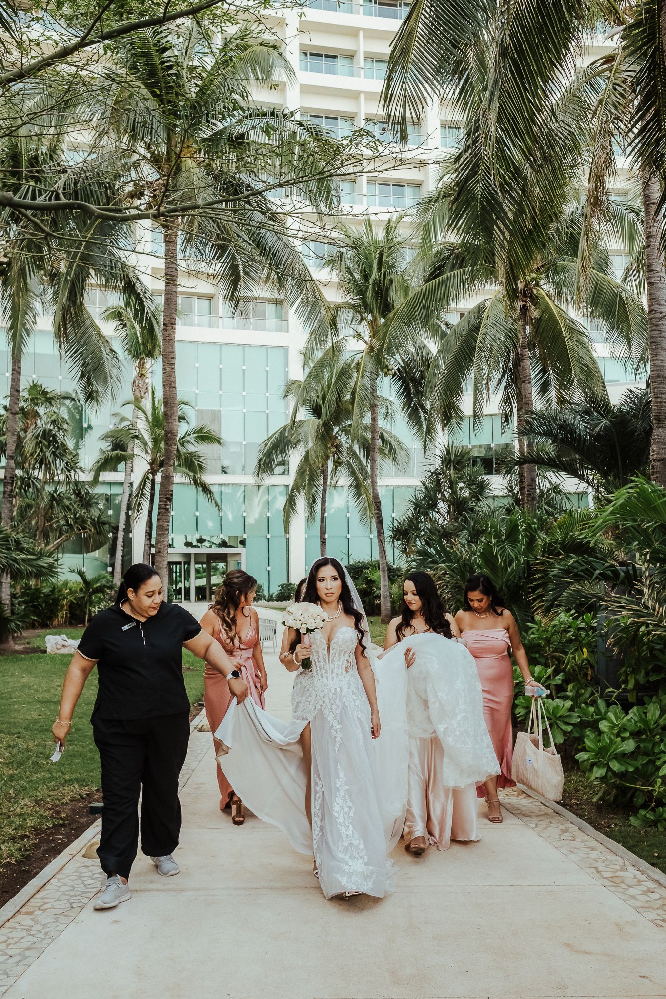 Wedding party walking outdoors among palm trees at a tropical resort venue.