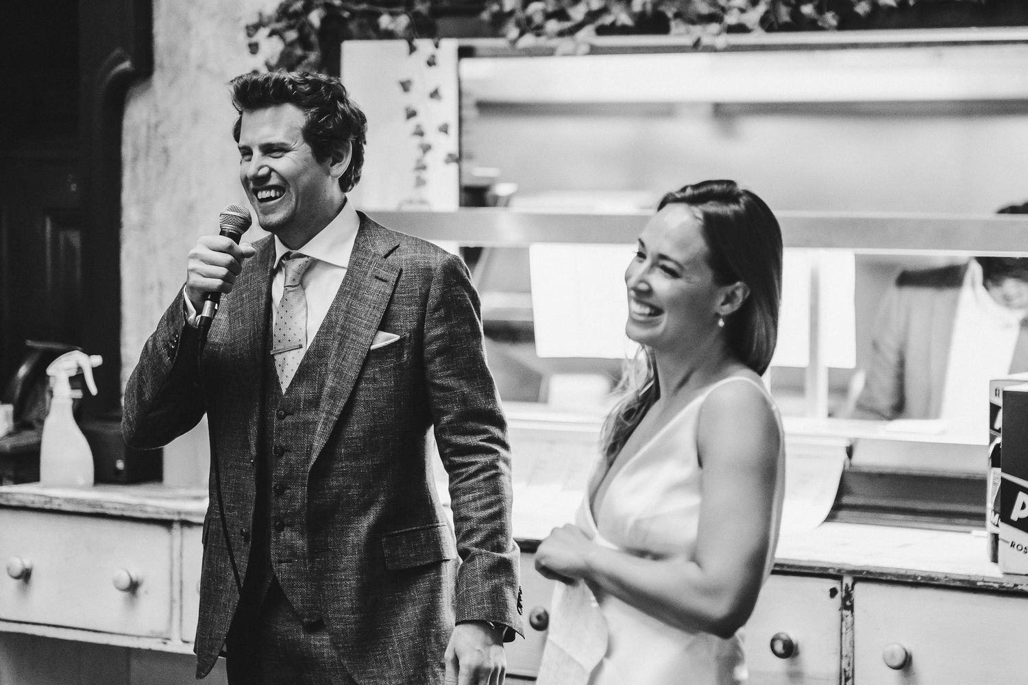 Wedding couple sharing speeches at an indoor reception with black and white photography.