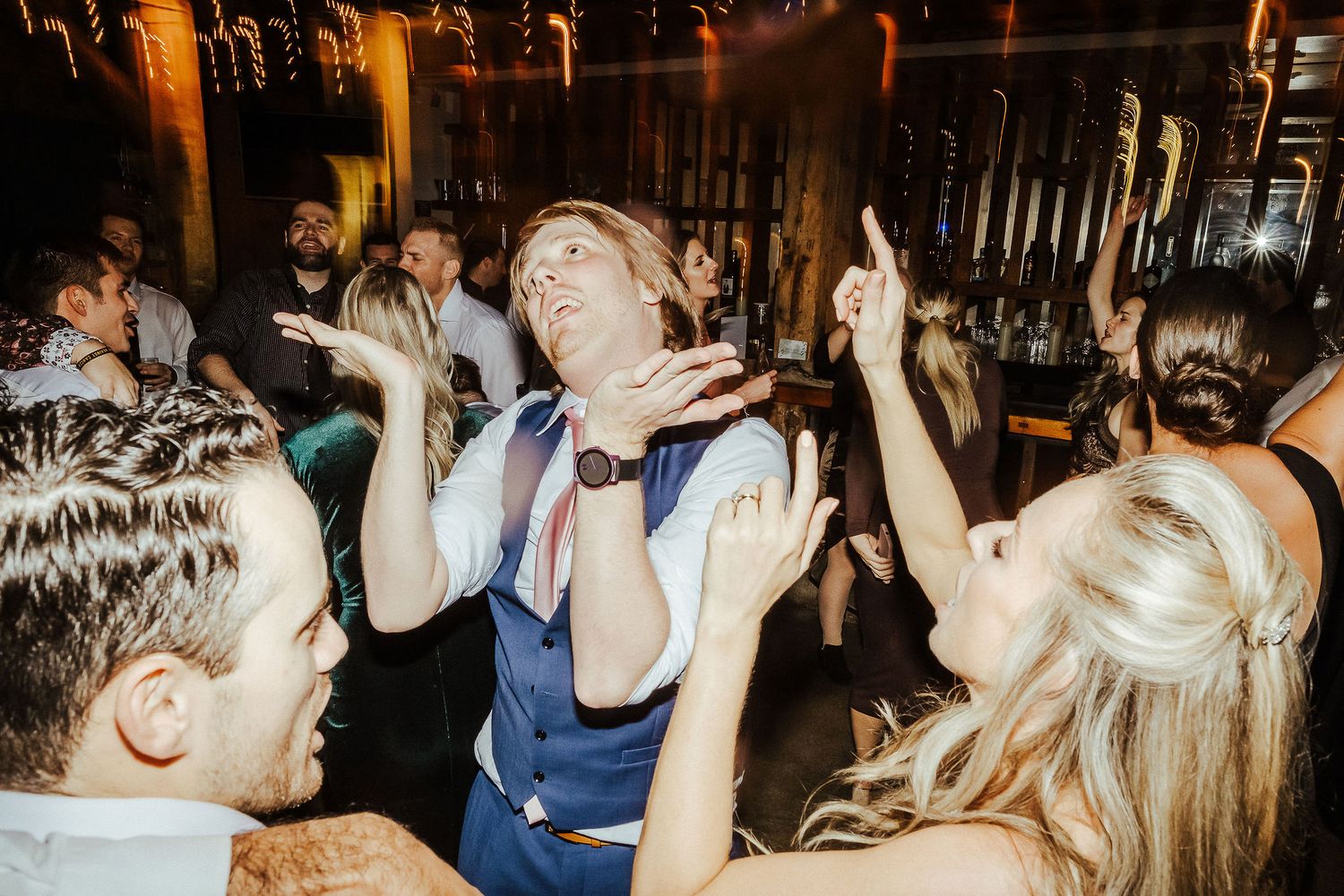 Wedding guests dancing energetically at reception celebration with dramatic party lighting.