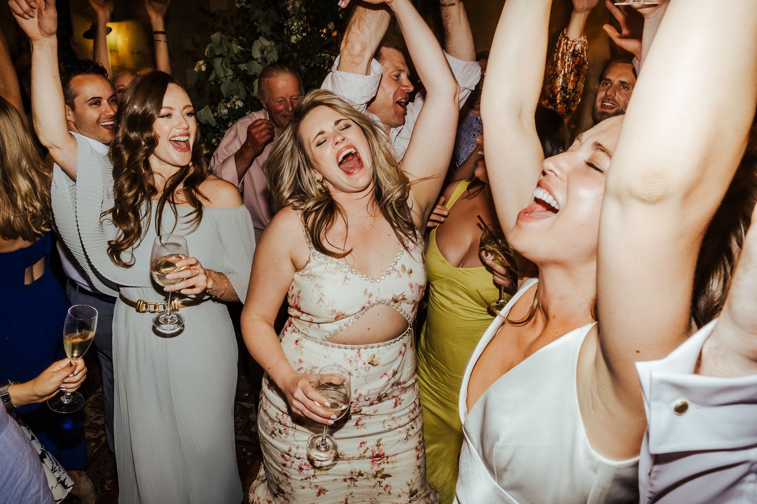 Wedding guests dancing with arms raised in celebration at a lively reception party.