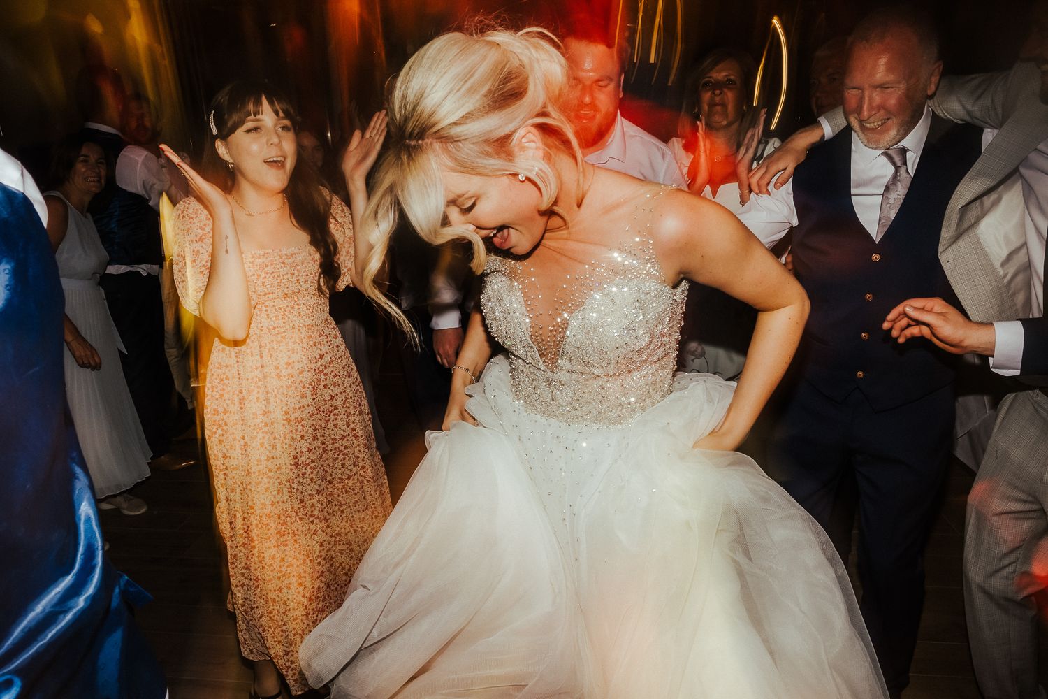 Bride in a tulle ballgown dances with joy during wedding reception under colorful lights.