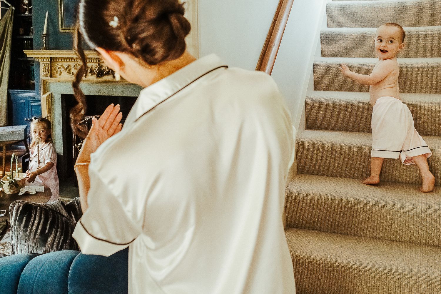 Candid moment of a young child playing on carpeted stairs while someone watches.