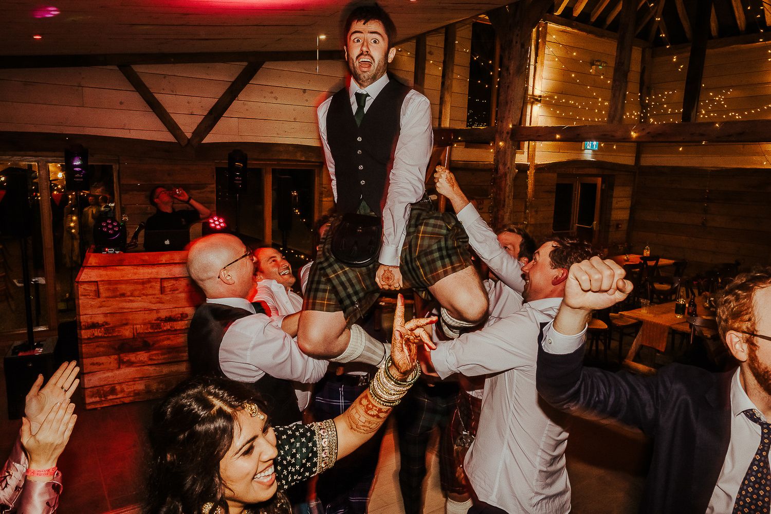 Groomsman being lifted by wedding guests during an energetic dance floor celebration.